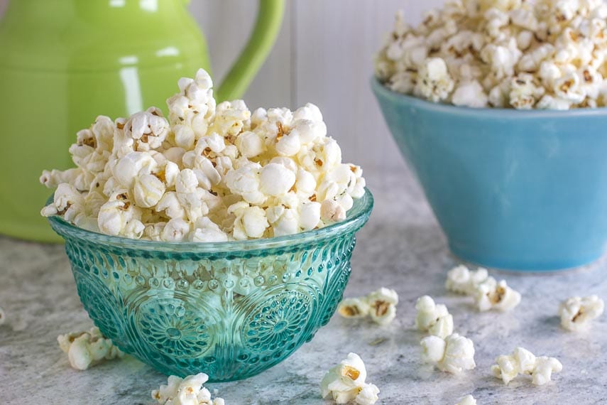 Garlicky Parmesan Herb Popcorn in clear teal glass bowl on gray quartz counter