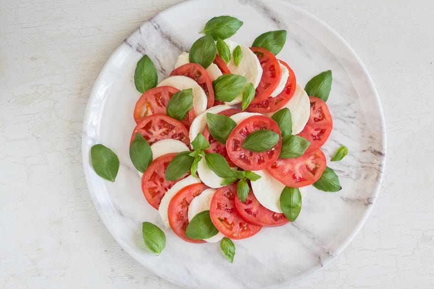caprese salad on marble dish on white wooden board