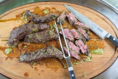 carving grilled hanger steak with Charmoula sauce on cutting board with Viking carving set