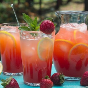 closeup of strawberry lemonade in clear glasses and pitcher, with sprig of mint