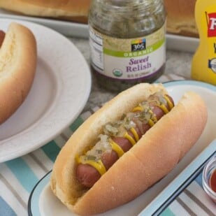 overhead image on two hot dogs on a white plate, with condiments