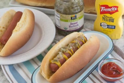 overhead image on two hot dogs on a white plate, with condiments