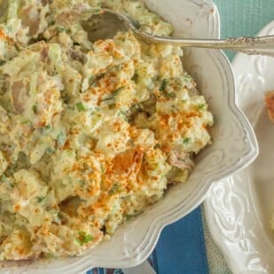 overhead shot of potato salad with hard boiled eggs in square white bowl with a silver serving spoon