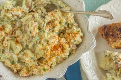 overhead shot of potato salad with hard boiled eggs in square white bowl with a silver serving spoon