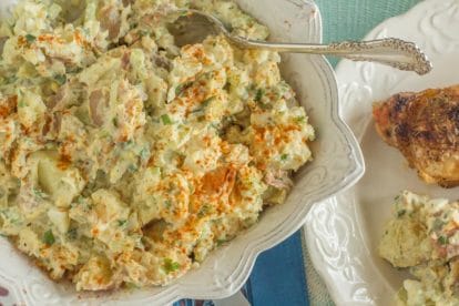 overhead shot of potato salad with hard boiled eggs in square white bowl with a silver serving spoon