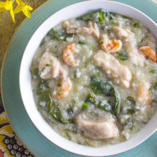 shrimp and chicken congee with greens in a white bowl on a blue plate