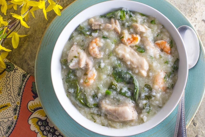 shrimp and chicken congee with greens in a white bowl on a blue plate