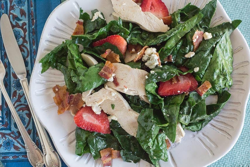 Spinach Salad with Hot Bacon Dressing, Chicken, Blue Cheese & Strawberries on a white plate with blue background