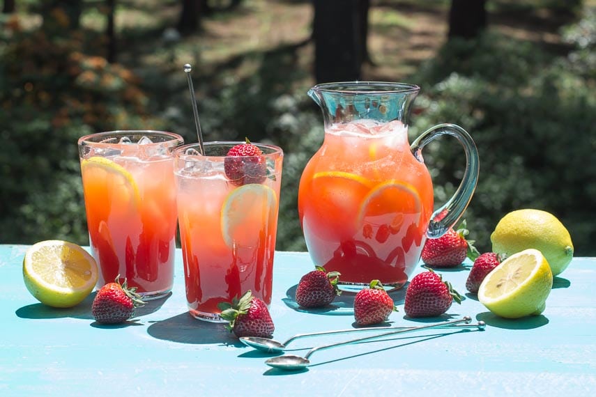 strawberry lemonade in pitcher and glasses on an aqua wooden board out on the deck in full sun