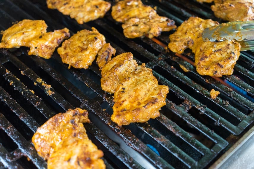using tongs to flip spiced Yogurt grilled chicken on the grill