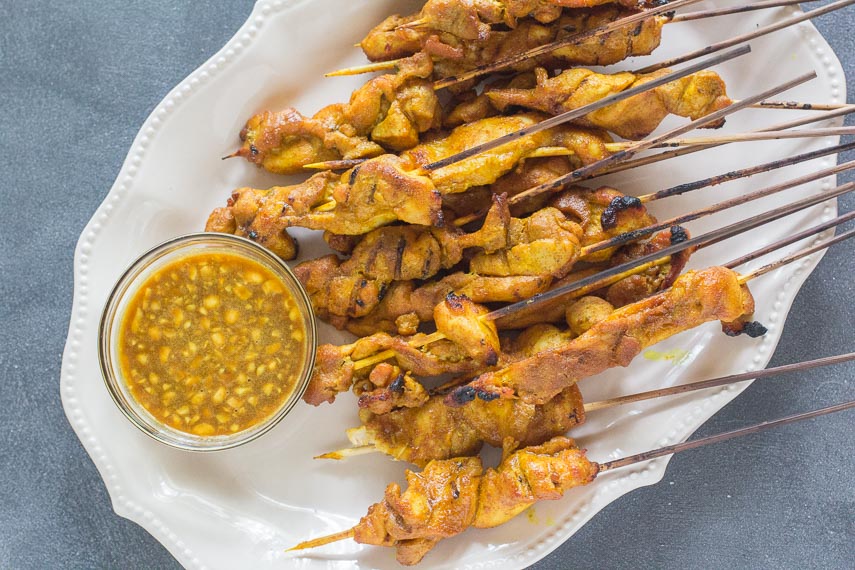closeup of Singapore Chicken Satay on white platter with dipping sauce in clear bowl