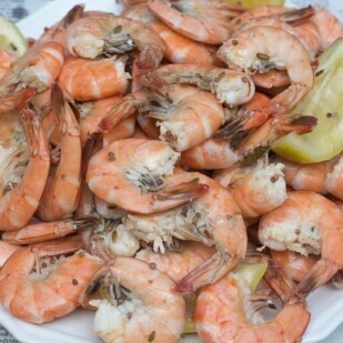 closeup of shrimp boil on white plate with lemon wedges