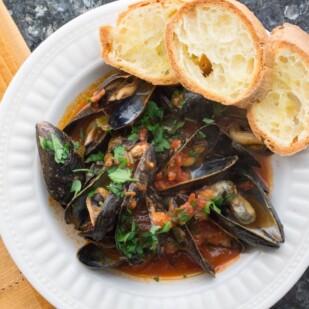Mussels with Tomatoes & White Wine with Garlic Toasts in a white bowl