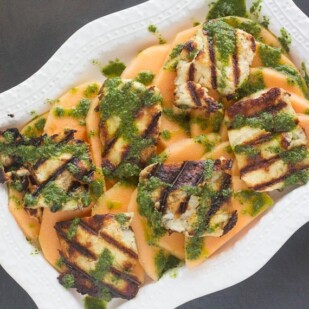 overhead image of grilled halloumi salad with melon on rectangular white platter