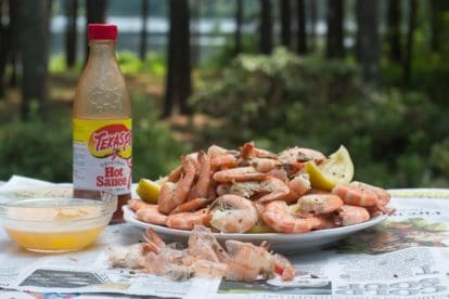 shrimp boil on white plate on top of newspaper on the deck