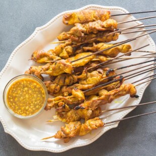 Singapore chicken satay on oval white platter with dipping sauce