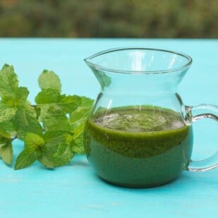 Low FODMP Mint salsa verde in glass pitcher with fresh mint alongside