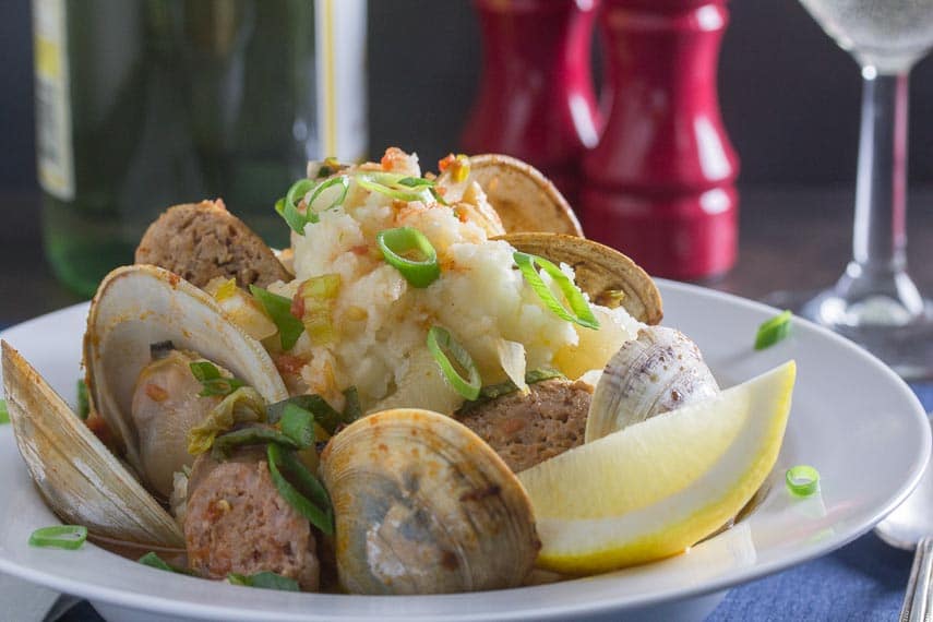 closeup of roast clams and spicy sausages with mashed potatoes in white bowl
