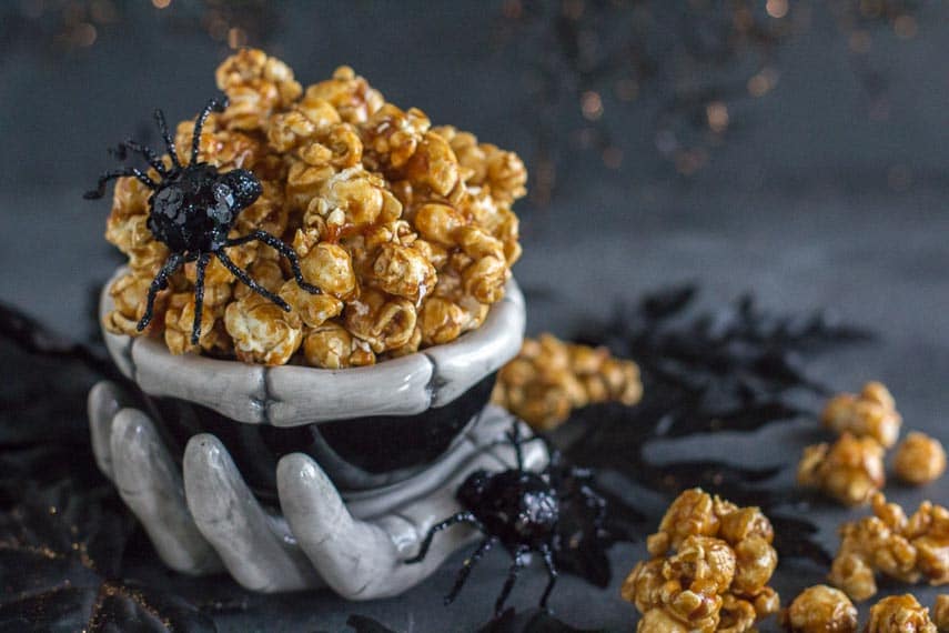 closeup of low FODMAP gingerbread caramel crunch popcorn in creepy ceramic skeleton bowl with black spiders