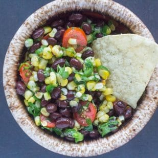 grilled corn salsa with black beans in a small bowl and a corn chip for dipping