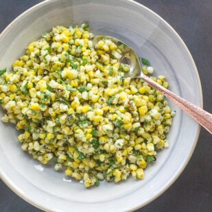 overhead of grilled corn salad with Parmesan and parsley on gray plate with serving spoon