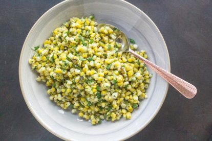 overhead of grilled corn salad with Parmesan and parsley on gray plate with serving spoon
