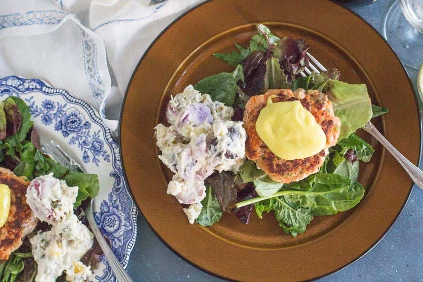 overhead of salmon burgers with aioli on a bed of greens and potato salad