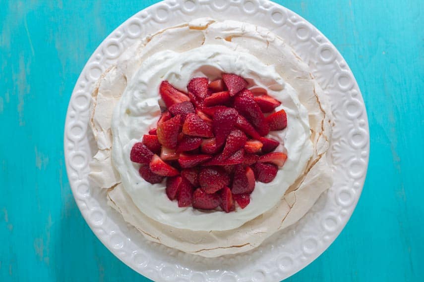 overhead shot of low FODMAP strawberry Pavlova on white plate against turquoise background