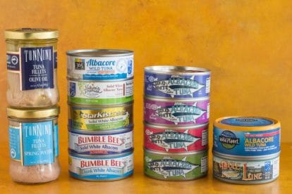 assorted cans and glass jars of tuna against a dark yellow background