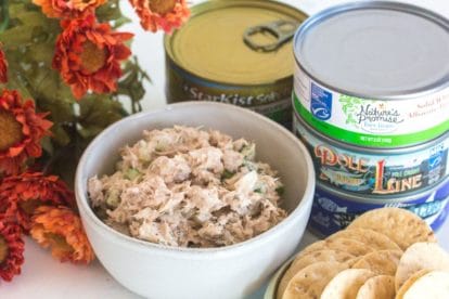 classic low FODMAP tuna salad in a small white bowl with cans of tuna in background