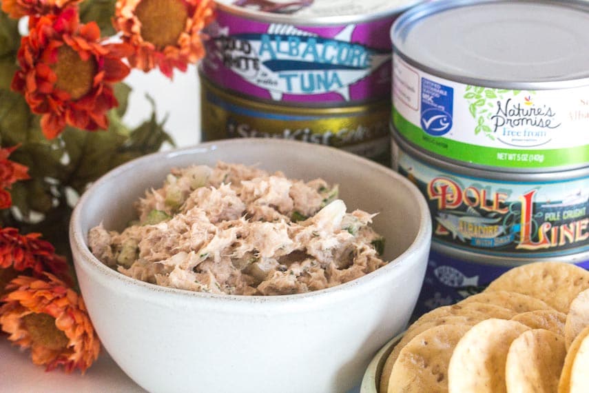 classic low FODMAP tuna salad in a small white bowl with cans of tuna in background