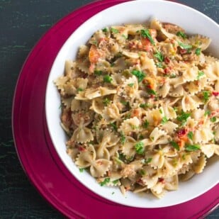 overhead image of Low FODMAP Pasta with Tuna & Sun Dried Tomatoes in white bowl on red plate
