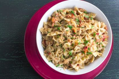 overhead image of Low FODMAP Pasta with Tuna & Sun Dried Tomatoes in white bowl on red plate