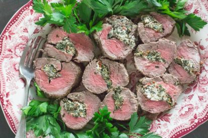 Overhead image of Beef Tenderloin Stuffed with Goat Cheese, Spinach & Sun-Dried Tomatoes on a red and white platter