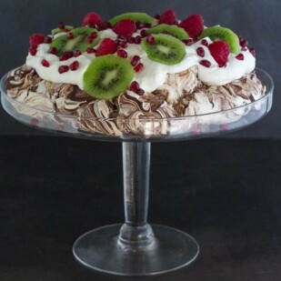 side view of Low FODMAP Chocolate Pavlova with Pomegranate, Raspberries & Kiwi in a glass pedestal dish