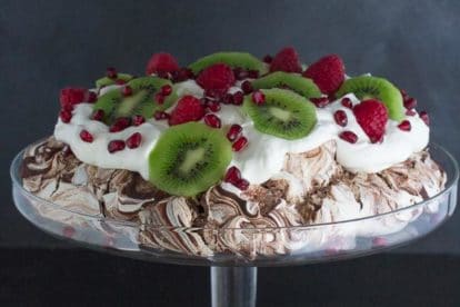 side view of Low FODMAP Chocolate Pavlova with Pomegranate, Raspberries & Kiwi in glass pedestal dish
