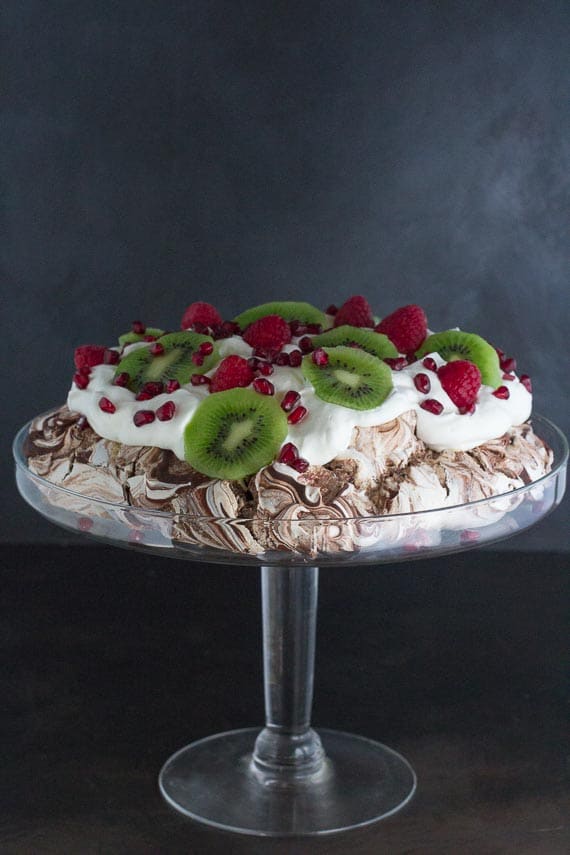 side view of Low FODMAP Chocolate Pavlova with Pomegranate, Raspberries & Kiwi in glass pedestal dish