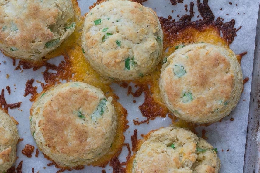 low fodmap cheddar scallion biscuits on baking sheet with parchment paper and melted cheese