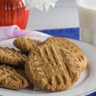 one bowl peanut butter cookies on a white plate with glass of lactose-free milk