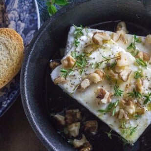 overhead image of baked feta with honey and walnuts and thyme in a cast-iron pan