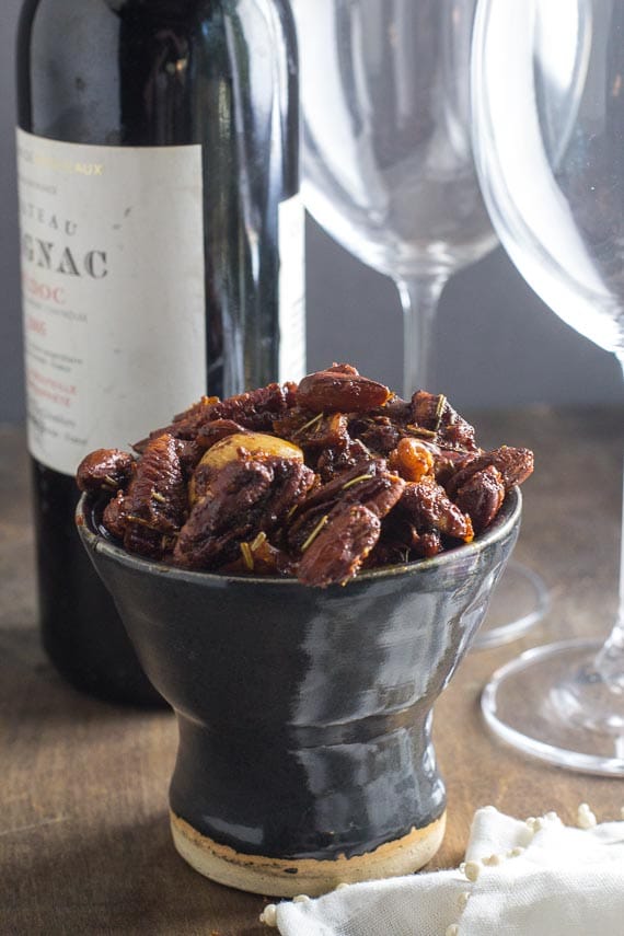 vertical image of easy low FODMAP sweet & Spicy nuts in a dark ceramic dish