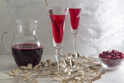 Low FODMAP Cranberry Cinnamon Swizzle in a champagne glass; cranberry juice in pitcher