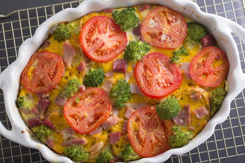 overhead of savory bread pudding in white oval casserole with broccoli and tomato