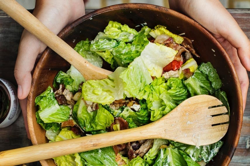 wooden salad bowl with salad and wooden spoon and fork, held in hands
