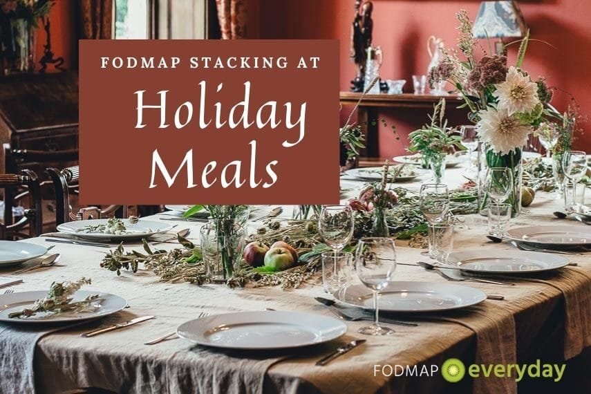 A dining table set for a holiday meal with white plates on a light brown table cloth, greenery and candle holders. With the text: FODMAP Stacking at Holiday Meals