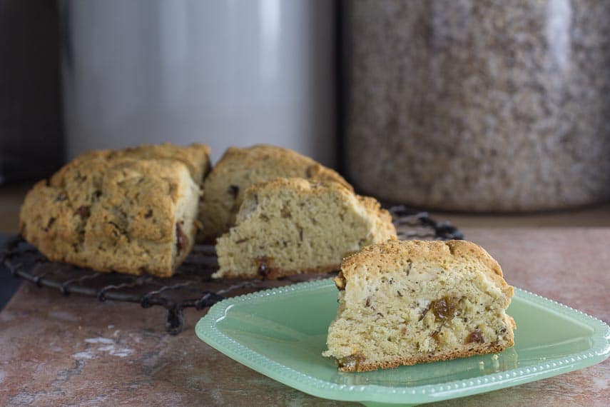 Rich low FODMAP Irish soda bread wedge on plate with loaf in background on rack