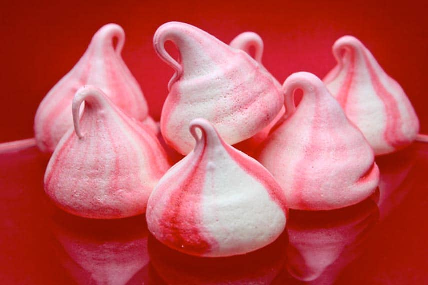 Low FODMAP Peppermint Meringues piped as kisses on red background. Gluten-Free Christmas Cookies everyone will love!