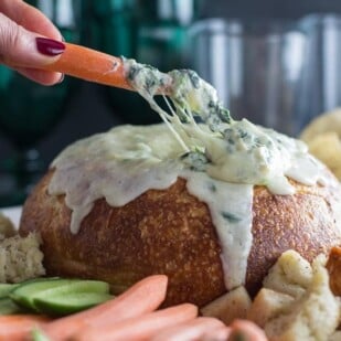cheesy low FODMAP hot spinach artichoke dip with carrot in hand dipping