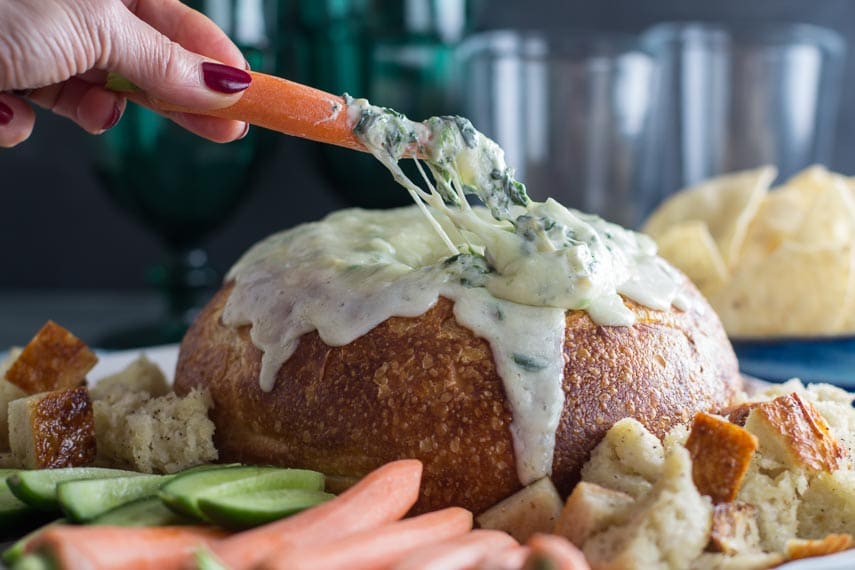 cheesy low FODMAP hot spinach artichoke dip with carrot in hand dipping