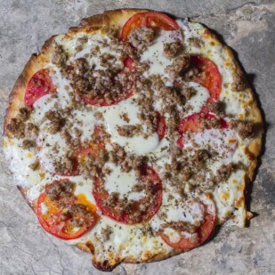 Low FODMAP CBD Oil Pizza with Sausage & Fresh Tomato on a stone surface